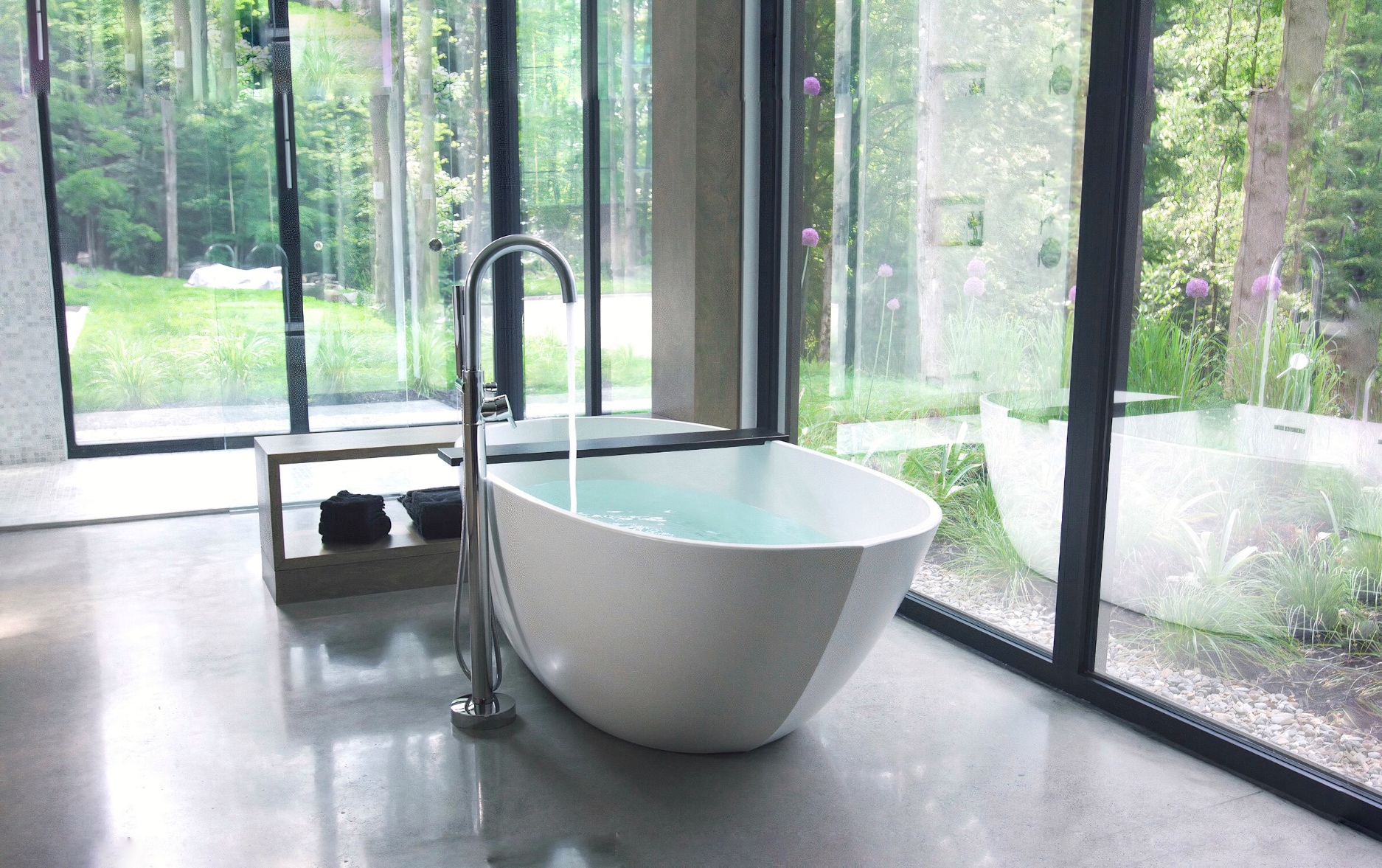 This bathroom features a white free-standing tub, a silver-finished faucet and large windows to overlook a view of nature.